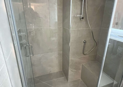 Tiled walk-in shower with rainfall showerhead, handheld shower and built-in ledge — bathroom renovation by Glanmore Construction