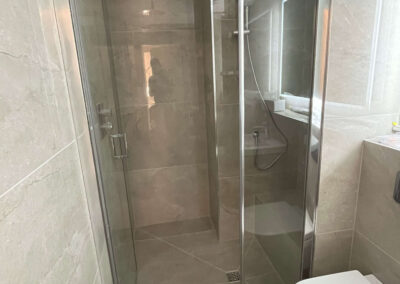 Modern tiled bathroom with walk-in glass shower and wall-mounted toilet — renovation by Glanmore Construction