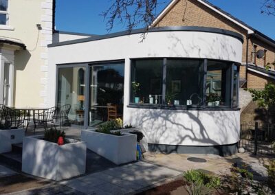 Modern curved rear house extension with full-height glazing, patio area and landscaped garden