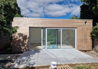 Newly built garden room with timber cladding, large sliding glass doors and tiled patio area