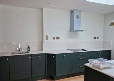 Modern renovated kitchen with matte green cabinets, white quartz countertops, induction hob and stainless steel extractor fan