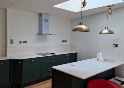 Renovated modern kitchen with skylight, brass pendant lights, green cabinetry and white quartz breakfast bar
