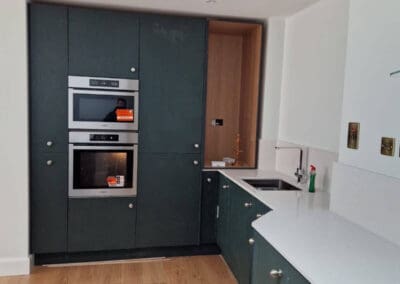 Modern renovated kitchen with custom dark green cabinetry, built-in appliances and white quartz worktops